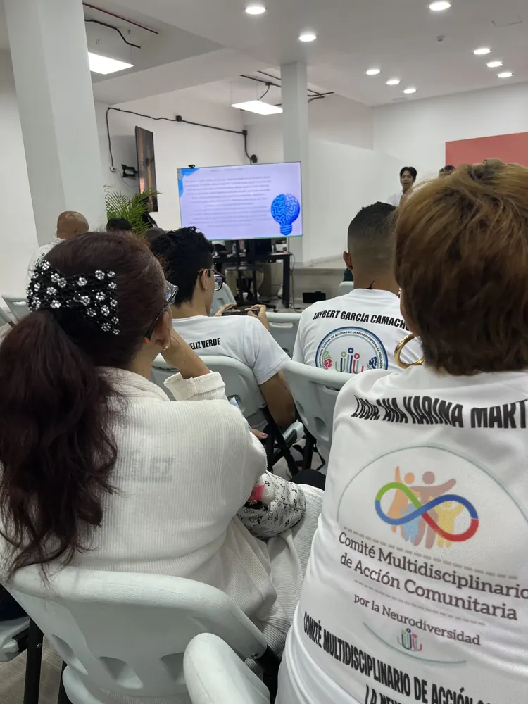 Participantes con camisas del Comité Multidisciplinario de Acción Comunitaria siguen una presentación en pantalla